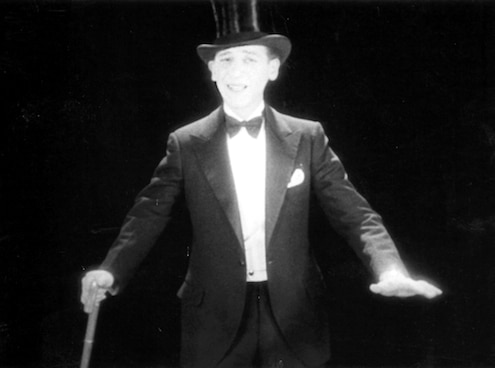 Man in tuxedo and top hat, mid-motion with cane