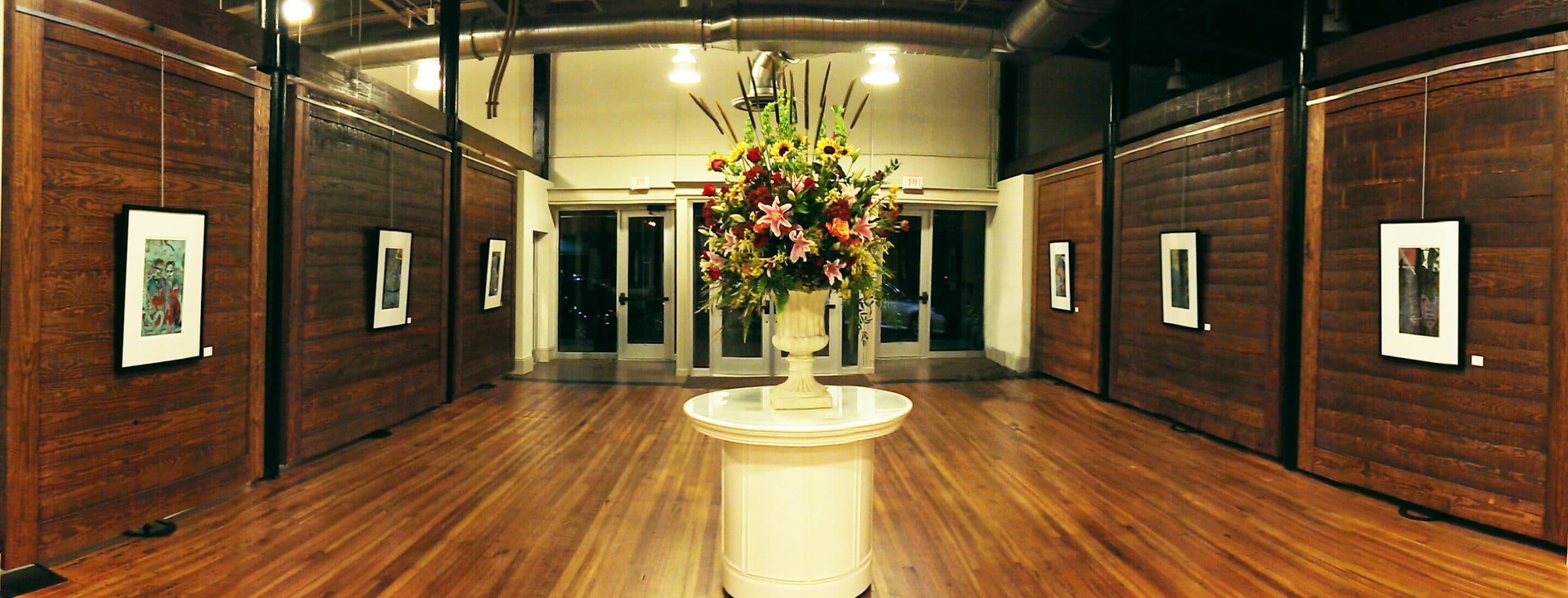 CAC Gallery room with wood floors and floral centerpiece on white pedestal.