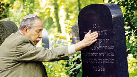 Elderly Jewish man having moment of meditation at tombstone in cemetery
