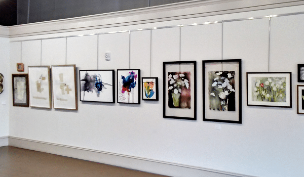 Row of artwork in frames hung on white gallery wall.