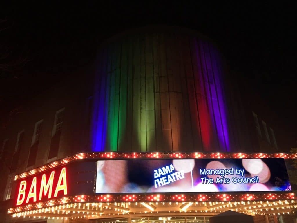 Bama Theatre marquee with rainbow lights lit up at night.