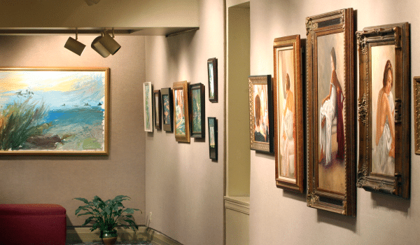 Row of paintings hung in gallery  in ornate frames.